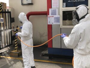 Matar Termite & Pest Control technicians in hazmat suits spraying near an entrance gate in Alexandria, VA.