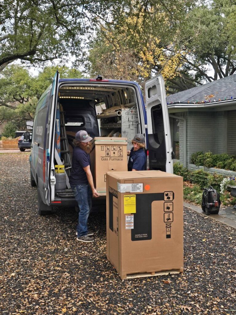 Two technicians unloading a new gas furnace from a company van for installation by Harlen Johnson Heating & Air in Dallas, TX.