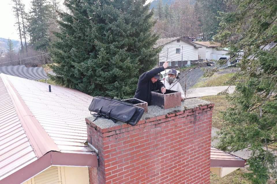 Two Chimney Wizards LLC technicians on a roof, actively working on a chimney flue during a sweep in Orofino, ID.