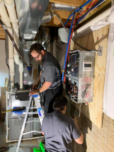 Two technicians working on a furnace and tankless water heater installation by Ash Plumbing, Drain & Sewer in Akron, OH.
