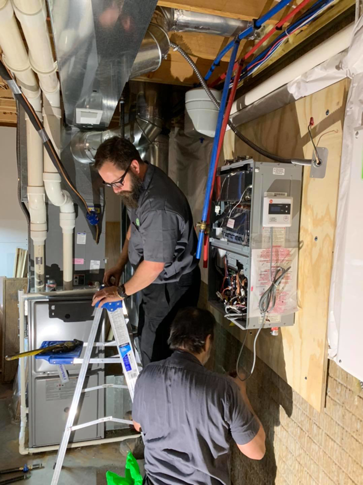 Two technicians working on a furnace and tankless water heater installation by Ash Plumbing, Drain & Sewer in Akron, OH.