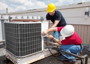 Two technicians working on a large rooftop AC unit for Greater Boston Heating & Air in Boston, MA.