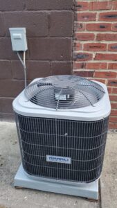 A Tempstar outdoor AC condenser unit installed next to a brick wall by R. Davis Mechanical in Pittsburgh, PA