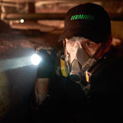 A Terminix technician inspecting a dark crawl space with a flashlight and respirator in Springfield, IL.