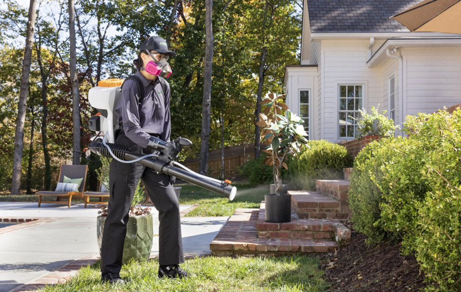 A Terminix technician in protective gear spraying for pests in a residential yard in Springfield, IL.