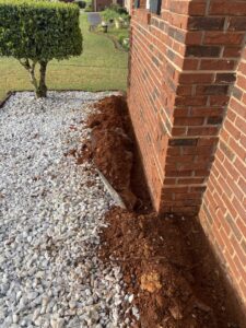 A trench dug along the brick foundation of a house, indicating a termite barrier treatment by Corsello & Son Pest Control Services in Atlanta, GA.