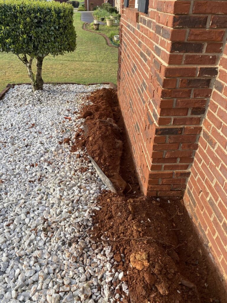 A trench dug along the brick foundation of a house, indicating a termite barrier treatment by Corsello & Son Pest Control Services in Atlanta, GA.