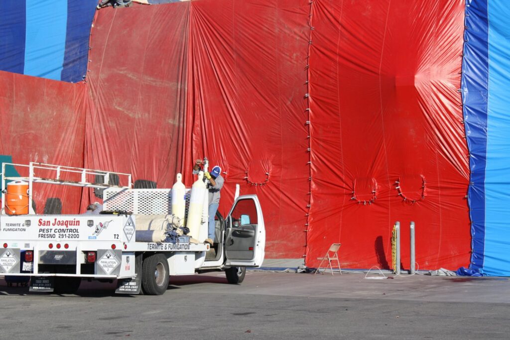 A San Joaquin Pest Control truck next to a building covered in red and blue tarps for termite fumigation in Fresno, CA.