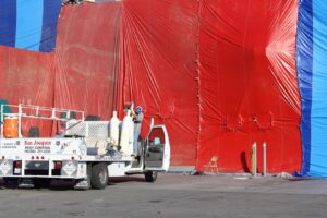 A San Joaquin Pest Control truck next to a building covered in red and blue tarps for termite fumigation in Fresno, CA.