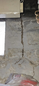 A long, thick termite mud tube running down a concrete foundation wall from a window sill, indicating pest control work by MJ's Absolute Solutions in Parma, OH.