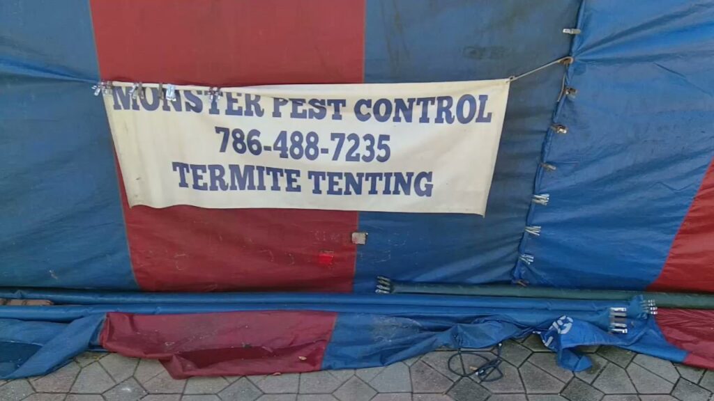 A close-up of the Monster Pest Control banner on a house tented for termite treatment in Miami, FL.