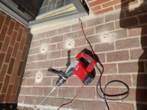 A hammer drill and drilled holes in a brick foundation for termite barrier treatment by EcoPro Termite & Pest in Dayton, OH