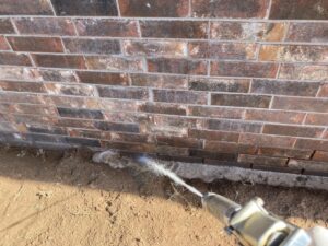 Close-up of a technician spraying liquid for termite treatment into the ground next to a brick foundation by Roach's Termite Service Inc. in Oklahoma City, OK