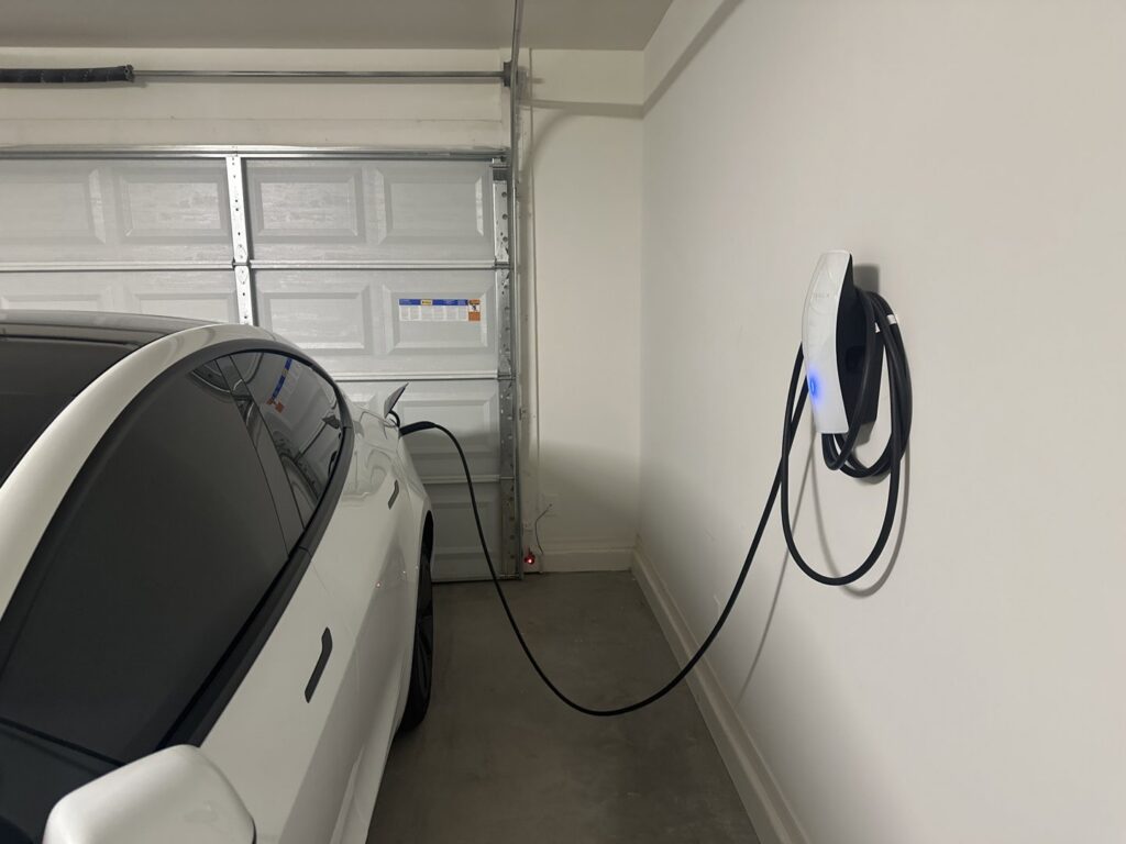 A white Tesla car charging in a garage from a wall-mounted EV charging station installed by Castle Electrical & Lighting in Scottsdale, AZ.