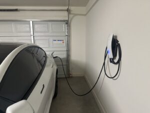 A white Tesla car charging in a garage from a wall-mounted EV charging station installed by Castle Electrical & Lighting in Scottsdale, AZ.