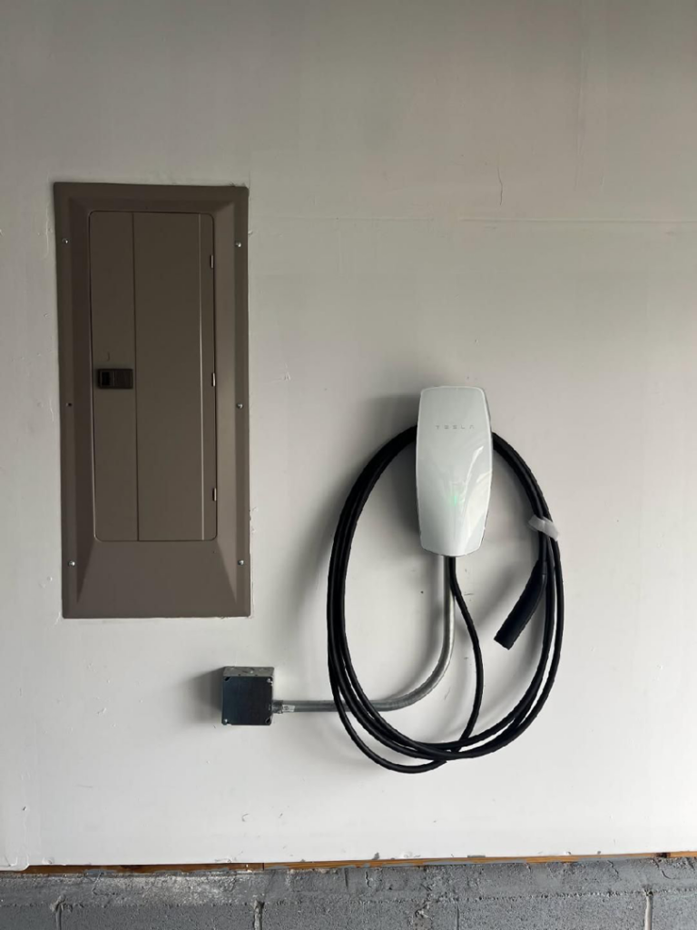 A newly installed Tesla EV charger and electrical panel on a white wall by Corey N Craig Electric LLC in Charlotte, NC.