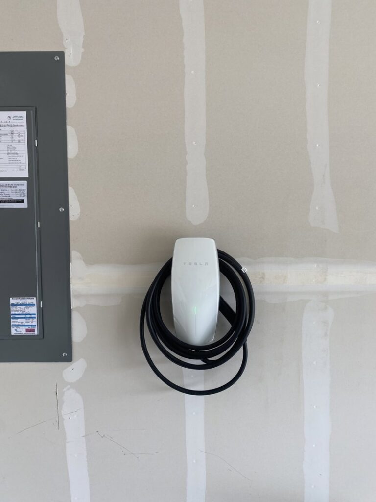 A Tesla EV charger installed on a garage wall next to an electrical panel, a service provided by Peak Electric in Mount Washington, KY.