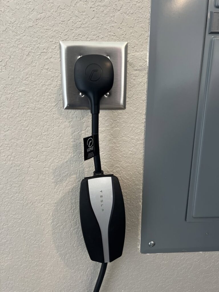 A Tesla EV charger plugged into an outlet next to an electrical panel, installed by Mister Sparky NWA in Springdale, AR.