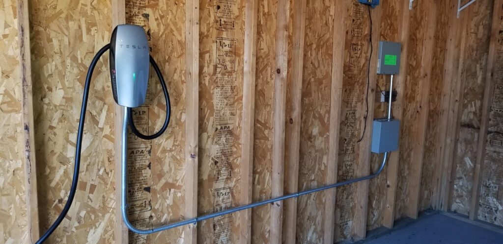 A Tesla EV charger installed on a wooden wall in a garage by Star Light Electric LLC in Phoenix, AZ