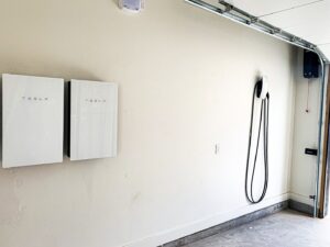 Two Tesla Powerwall battery storage units and a Tesla EV charger installed in a garage by Premier Power in Edmond, OK.