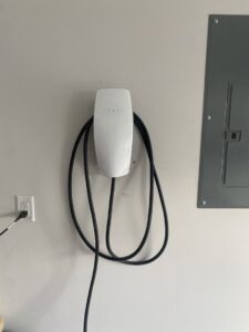 A Tesla Wall Connector EV charger installed on a wall next to an electrical panel by Ultralight Electric in Houston, TX.