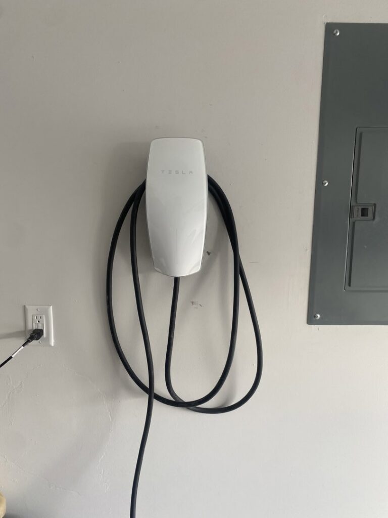 A Tesla Wall Connector EV charger installed on a wall next to an electrical panel by Ultralight Electric in Houston, TX.