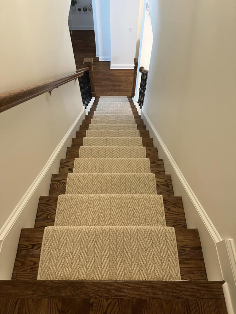 A newly installed light-colored, textured carpet runner on a dark wood staircase by On Point Flooring in Concord, NC