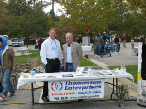 Two representatives from Thomasson Enterprises at an HVAC contractor promotional event in Portsmouth, VA, with a heating and cooling display.