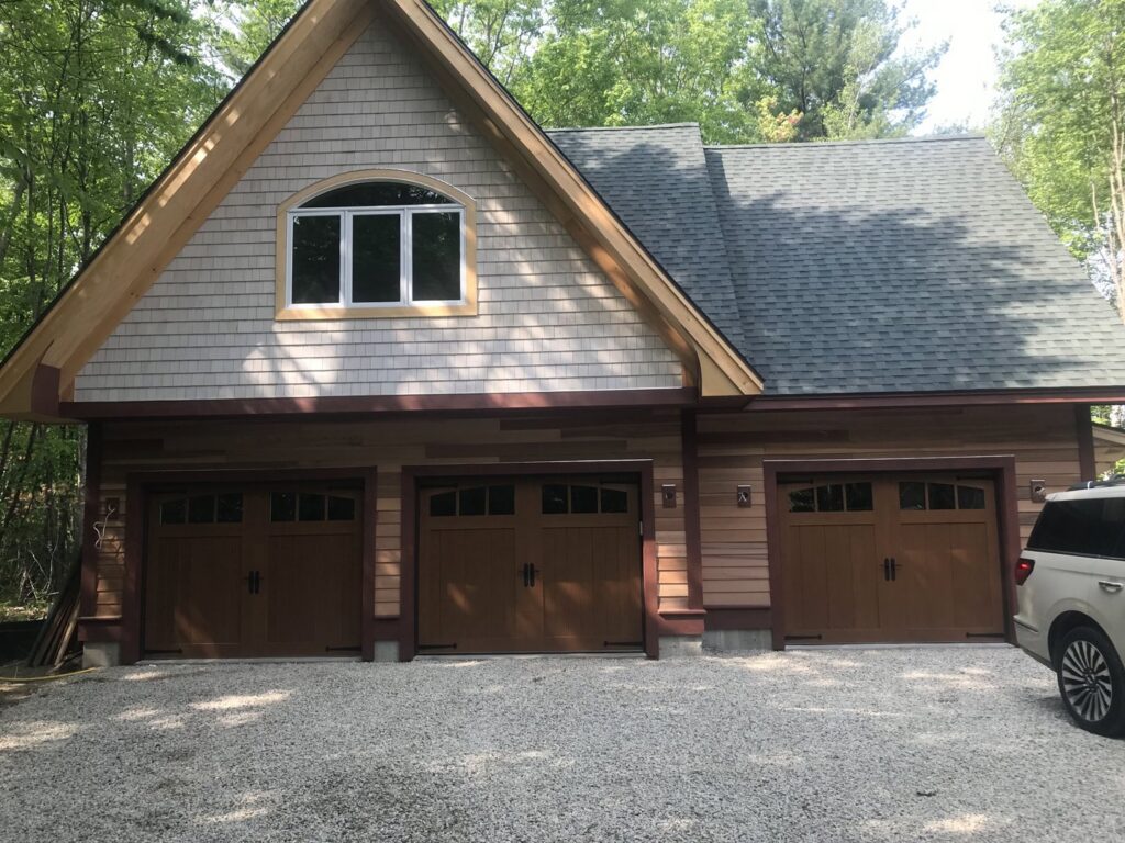 Three brown wood-look garage doors with windows installed on a house by PM Garage Door in Hudson, NH.