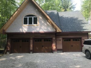 Three brown wood-look garage doors with windows installed on a house by PM Garage Door in Hudson, NH.