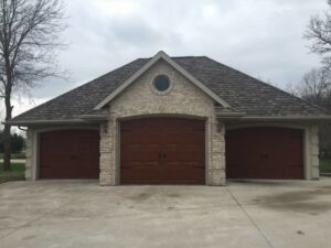Three brown residential garage doors on a brick house, installed by Tri County Overhead Door Service Inc in New London, WI.