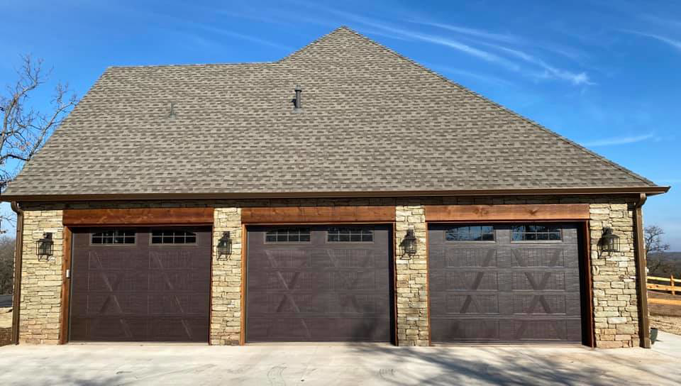 Three dark brown garage doors with windows installed on a stone facade home by Native Roots of Oklahoma in Edmond, OK