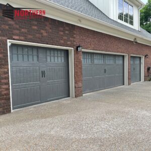 Three newly installed gray garage doors with decorative hardware on a brick house by Northern Door Company in Murfreesboro, TN