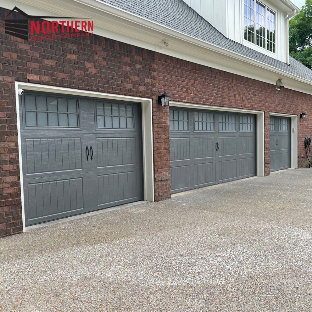 Three newly installed grey residential garage doors on a brick house by Northern Door Company in Saint Paul, MN
