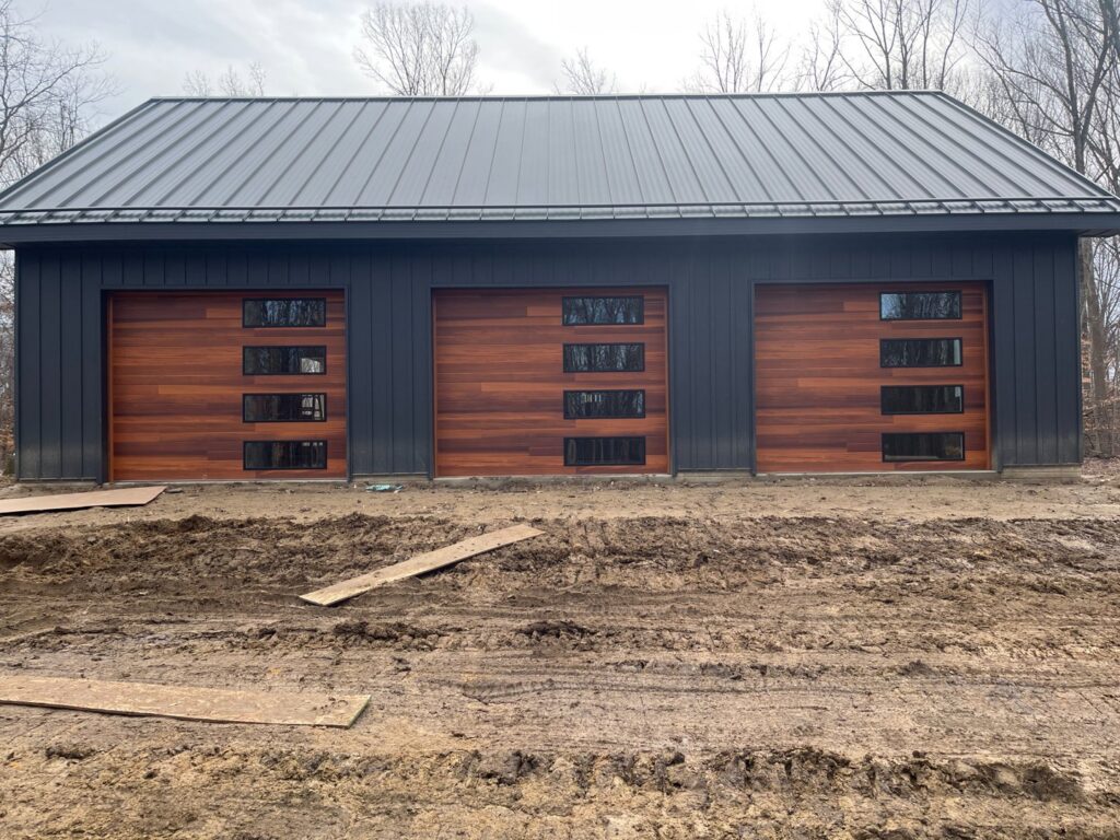 Three modern wooden garage doors with horizontal windows on a dark building, installed by Steve's Overhead Door Company in Lafayette, IN.
