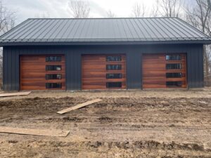 Three modern wooden garage doors with horizontal windows on a dark building, installed by Steve's Overhead Door Company in Lafayette, IN.