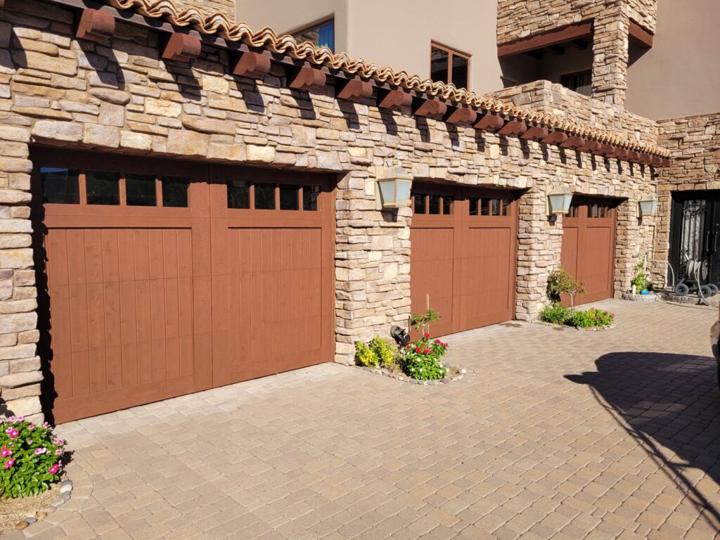 Three newly installed brown garage doors on a beautiful stone house, a project by JT's Overhead Doors in Gilbert, AZ.