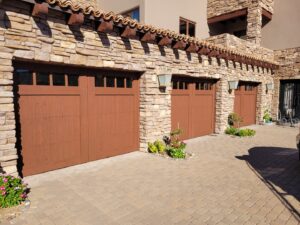 Three newly installed brown garage doors on a beautiful stone house, a project by JT's Overhead Doors in Gilbert, AZ.