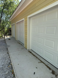 Three new white panel garage doors installed on a yellow-sided building by Up Garage Door in Nashville, TN.