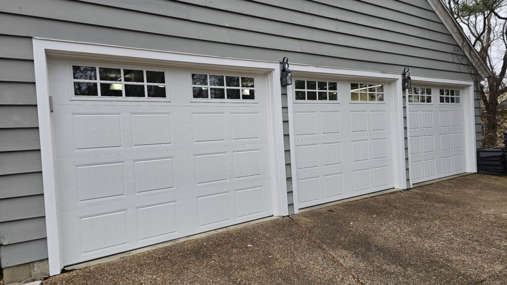 Three white garage doors with windows on a gray-sided house, installed by A+ Garage Door Repair in Evansville, IN.