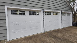 Three white garage doors with windows on a gray-sided house, installed by A+ Garage Door Repair in Evansville, IN.