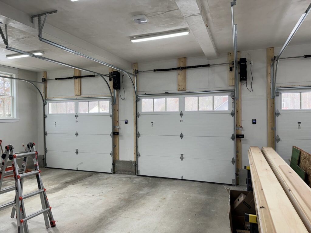Interior view of a garage with three white garage doors and openers installed by PM Garage Door in Hudson, NH.