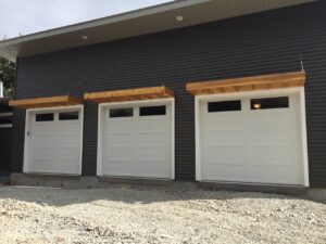 Three white modern residential garage doors installed on a dark gray house by Tri County Overhead Door Service Inc in New London, WI