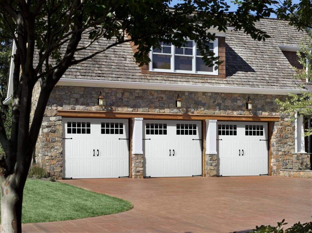 Three white traditional garage doors with windows on a stone house, installed by CCM Overhead Doors in Oklahoma City, OK.