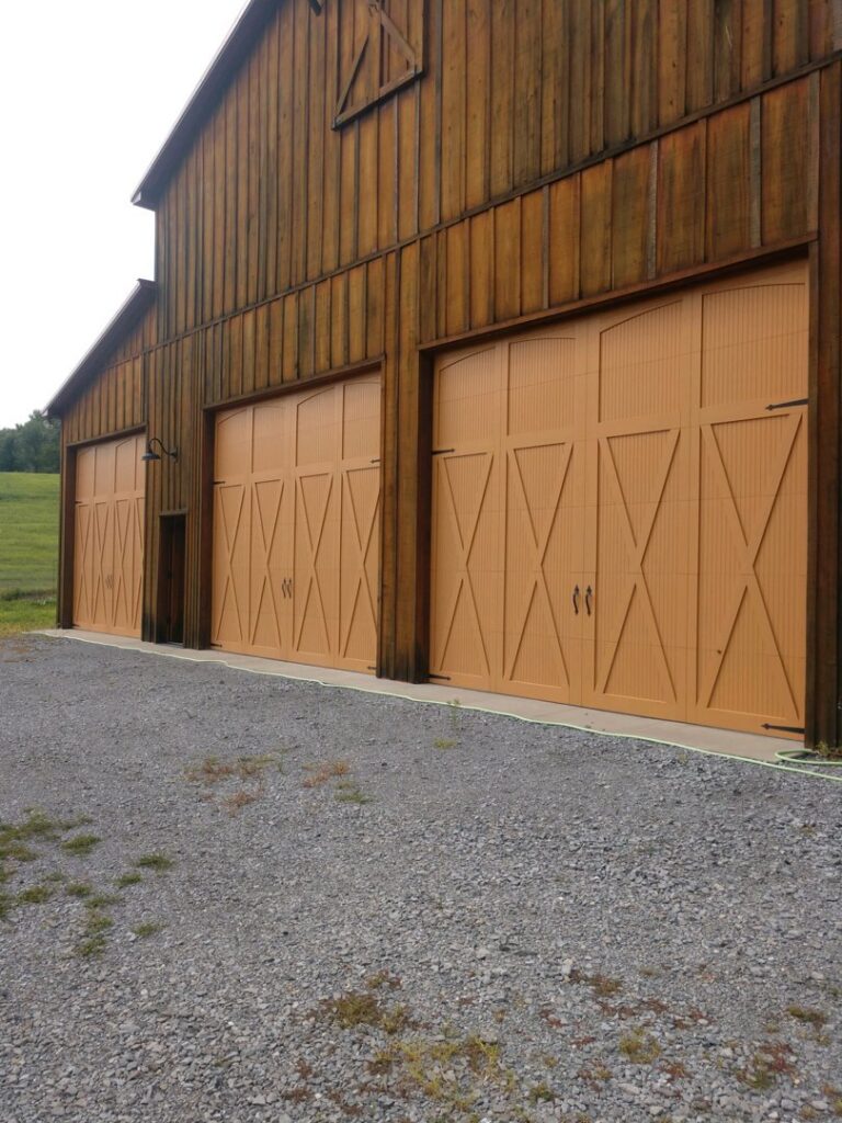 Three wood-look garage doors installed on a barn-style building by Ken's Overhead Door in Clarksville, TN.