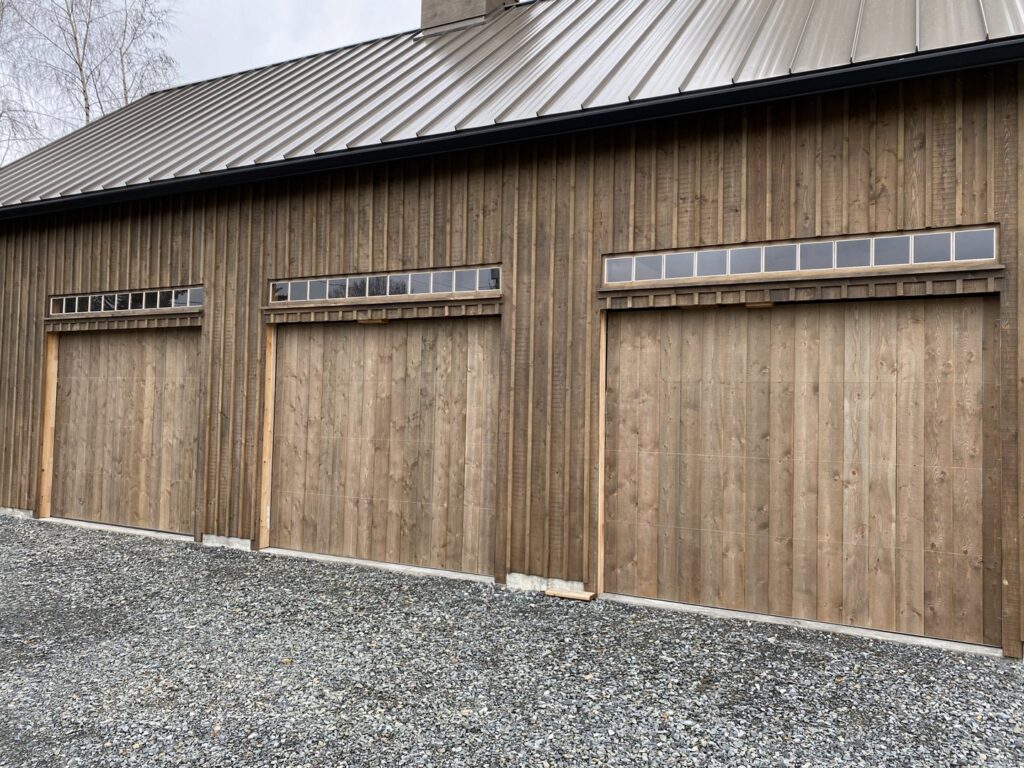 Three wooden garage doors with small windows installed on a barn-style building by Independent Garage Doors LLC in Tacoma, WA.