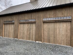 Three wooden garage doors with small windows installed on a barn-style building by Independent Garage Doors LLC in Tacoma, WA.