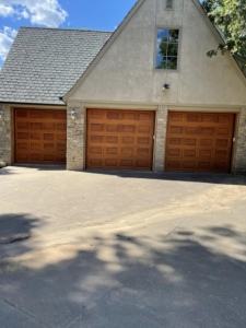 Three matching wooden panel garage doors installed on a house by L & S Overhead Door in Tulsa, OK.