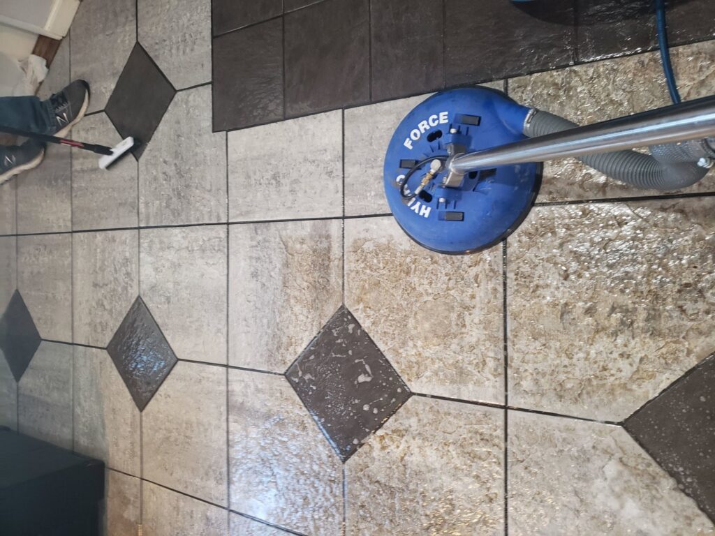 A blue rotary machine cleaning tile and grout flooring in progress by STC Carpet Care in Arvada, CO