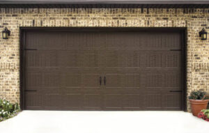 A traditional brown garage door with decorative hardware installed on a brick residential house by Overhead Doors Unlimited, LLC in Appleton, WI.